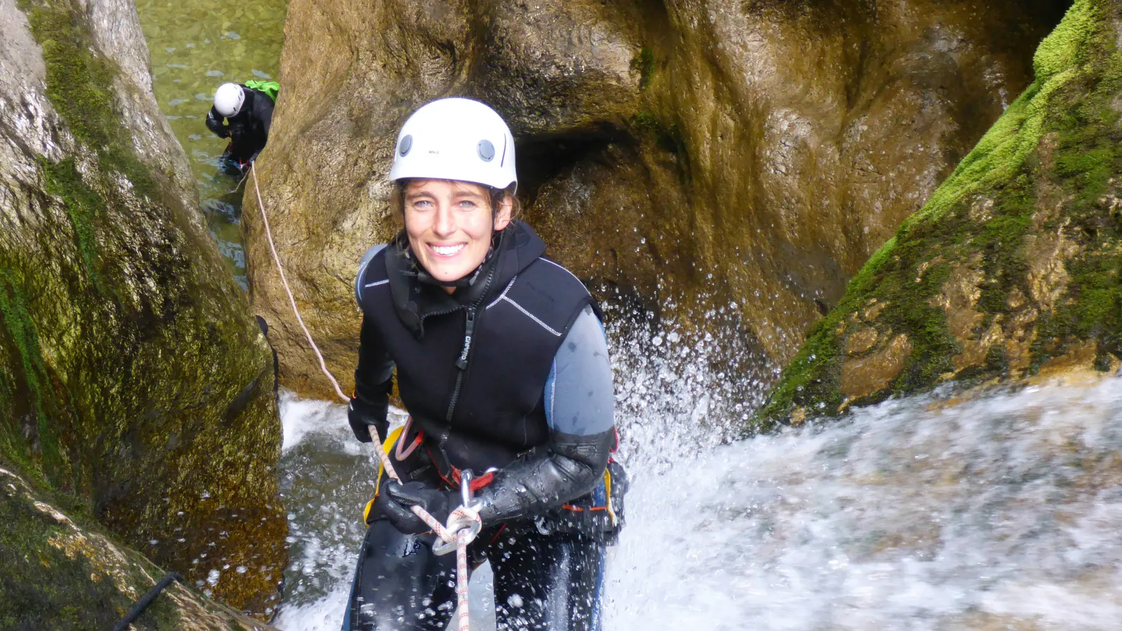 Eine Canyonautin seilt sich lächelnd in einem Wasserfall ab.
