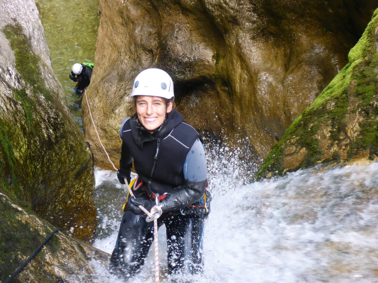 Eine Canyonautin seilt sich lächelnd in einem Wasserfall ab.