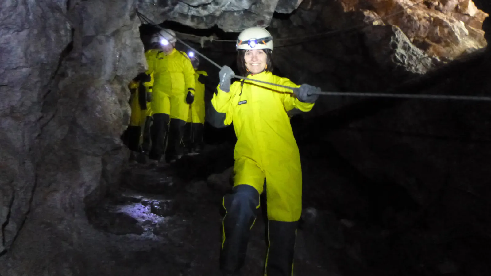 Eine Person im Höhlenanzug, die sich in der Höhle an einem Seil anhält.