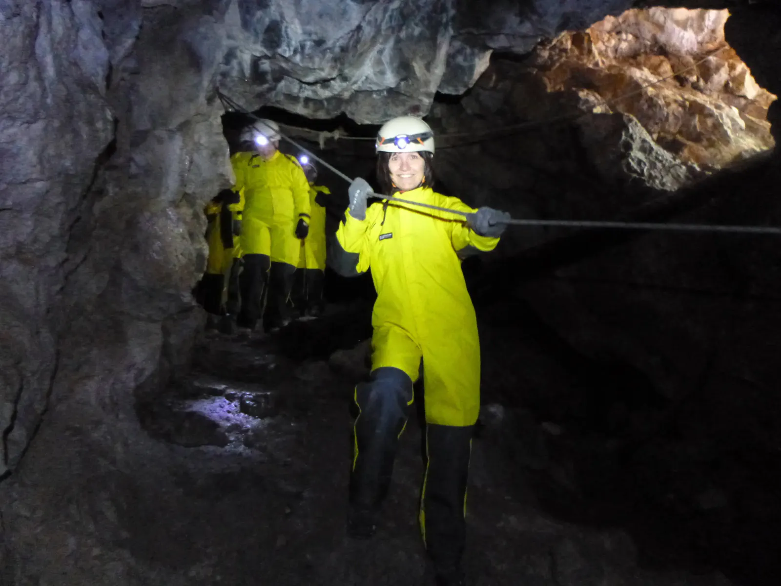Eine Person im Höhlenanzug, die sich in der Höhle an einem Seil anhält.