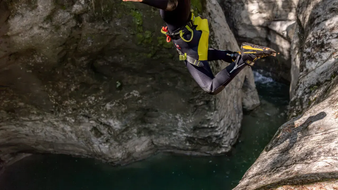 Frau springt in Canyoningausrüstung von Fels ins Wasser