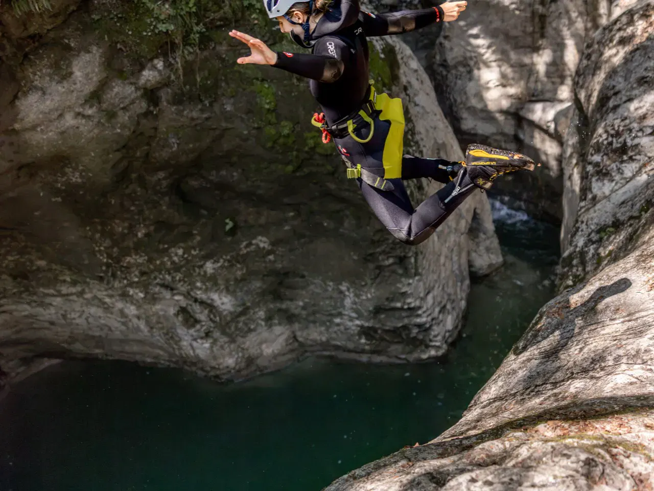 Frau springt in Canyoningausrüstung von Fels ins Wasser