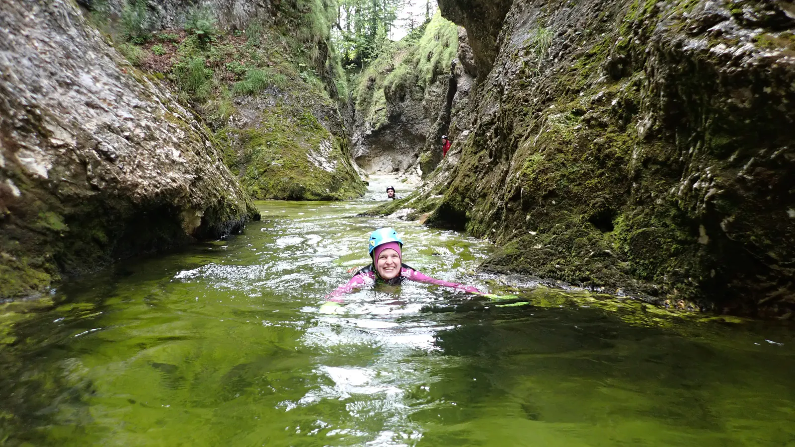 Eine Person schwimmt in einem Canyon zwischen moosbewachsenen Felsen.