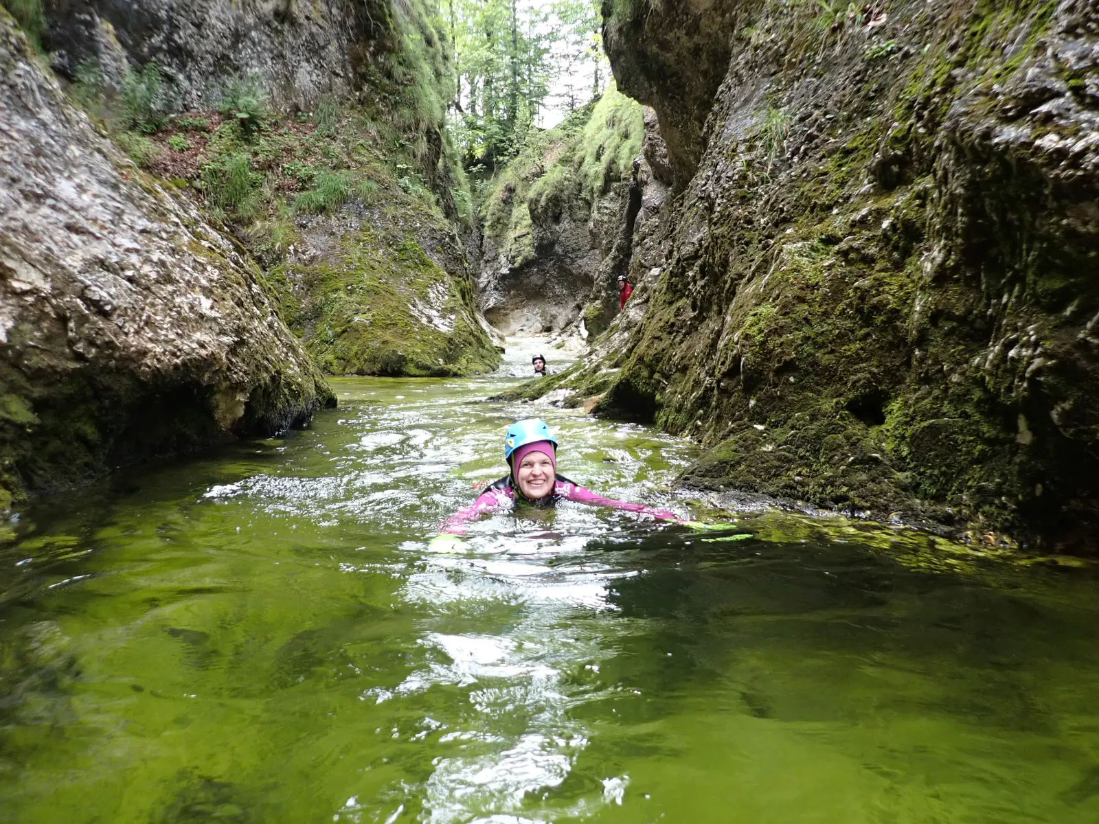 Eine Person schwimmt in einem Canyon zwischen moosbewachsenen Felsen.