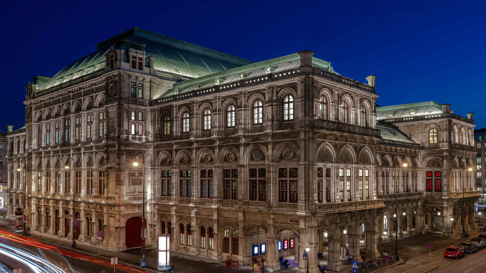 Wiener Staatsoper bei Nacht mit beleuchteter Fassade und Lichtspuren des Verkehrs.