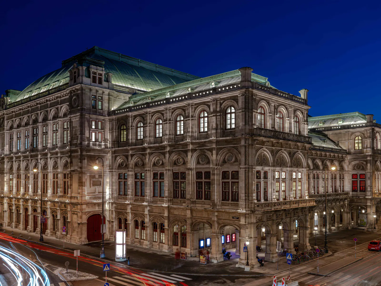 Wiener Staatsoper bei Nacht mit beleuchteter Fassade und Lichtspuren des Verkehrs.