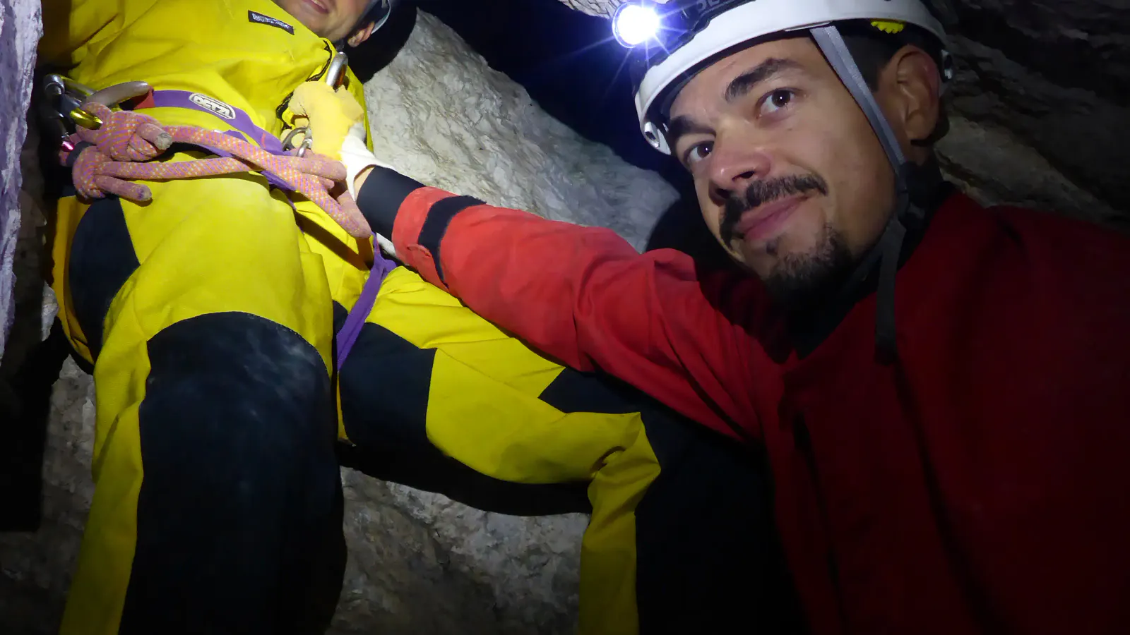 Zwei Personen mit Höhlenanzügen, Helmen und Stirnlampen in der Höhle.