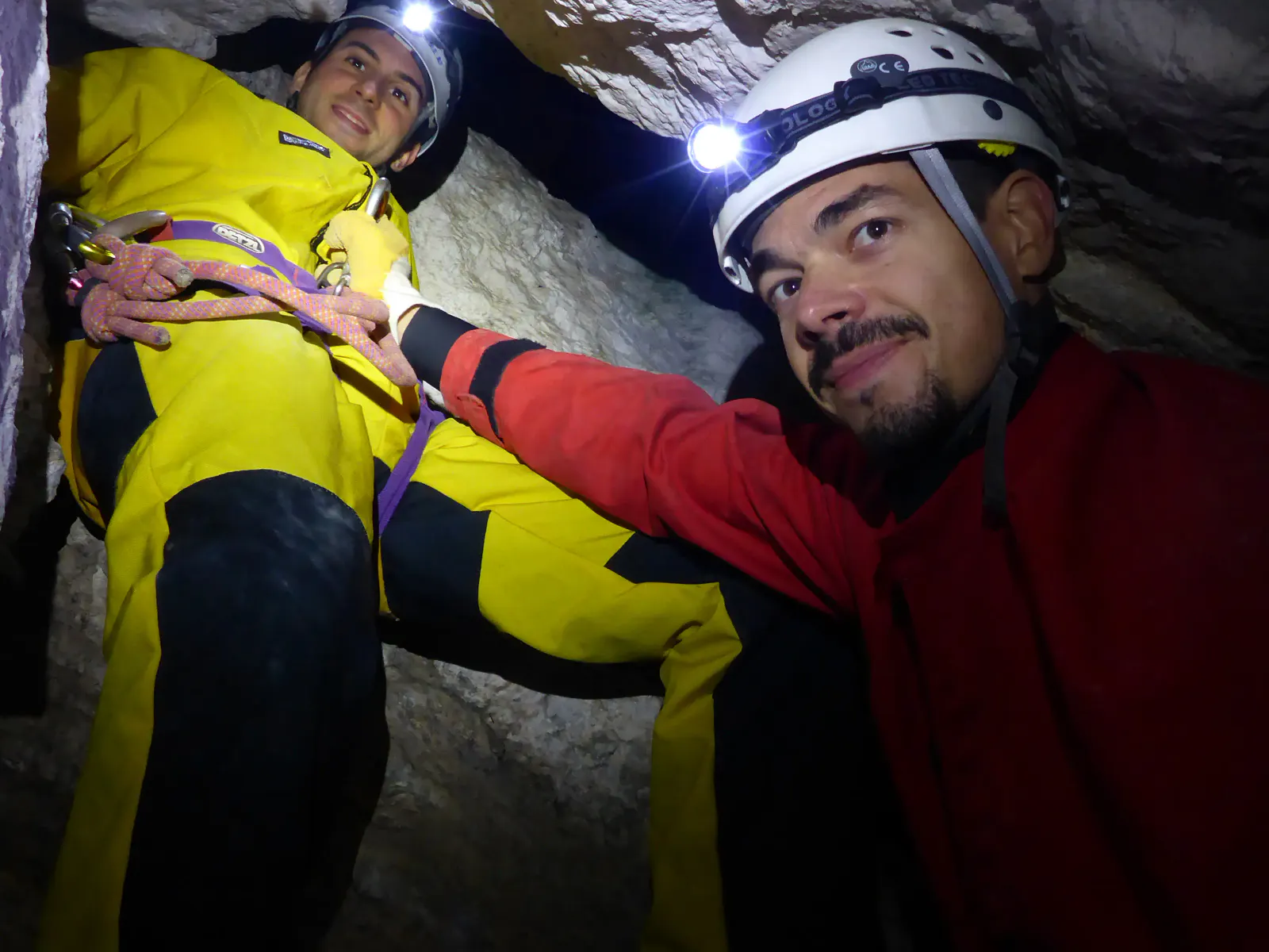 Zwei Personen mit Höhlenanzügen, Helmen und Stirnlampen in der Höhle.
