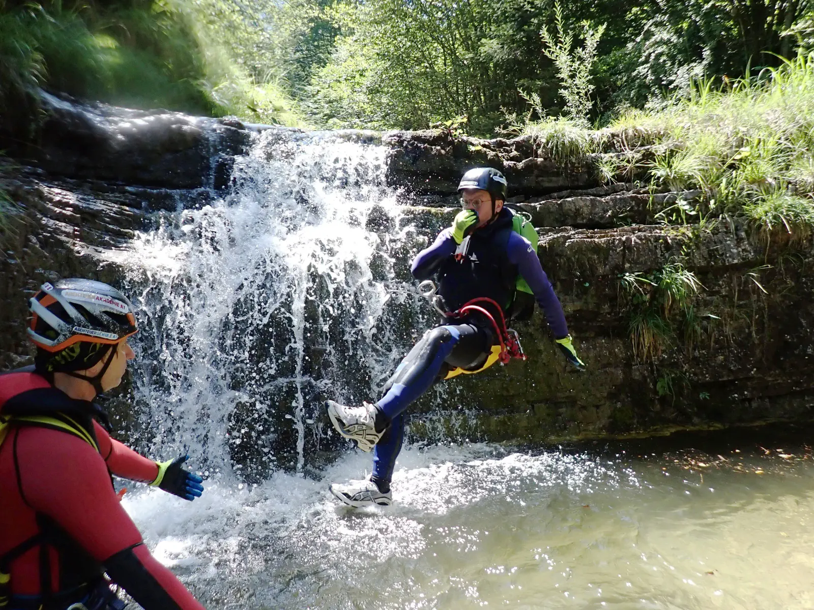 Eine Person im Flug bevor sie im Wasser landet mit einem kleinen Wasserfall im Hintergrund.