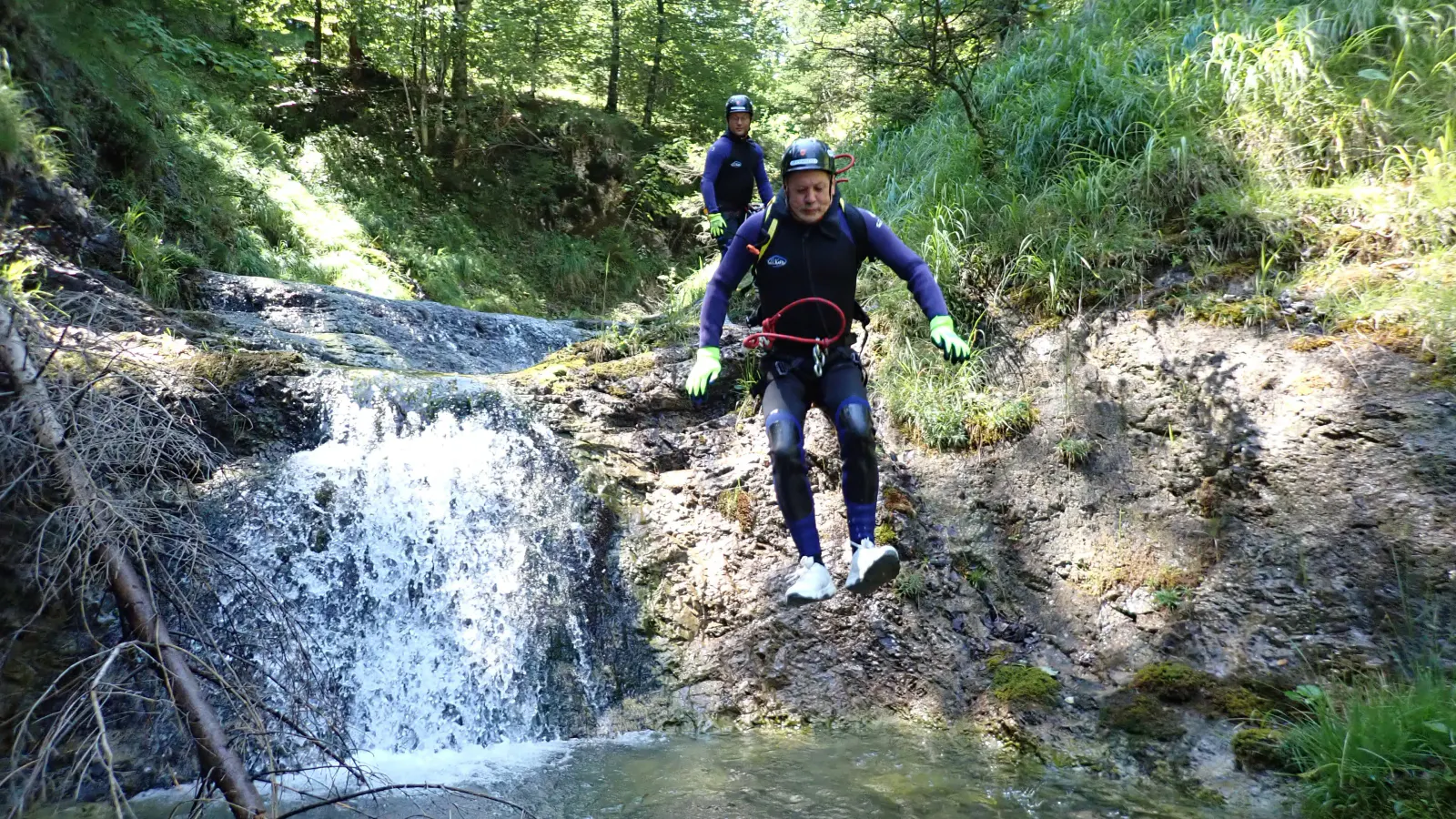 Eine Person springt von einem Vorsprung ins Wasser mit einem kleinen Wasserfall im Hintergrund