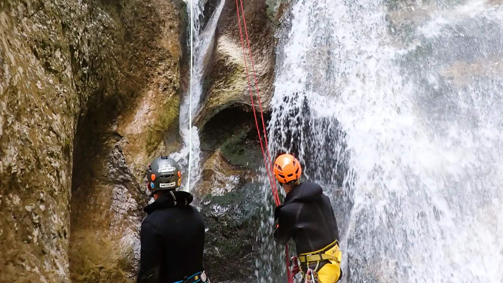 Ein Canyonaut wird von einem anderen in einem Wasserfall abgeseilt.