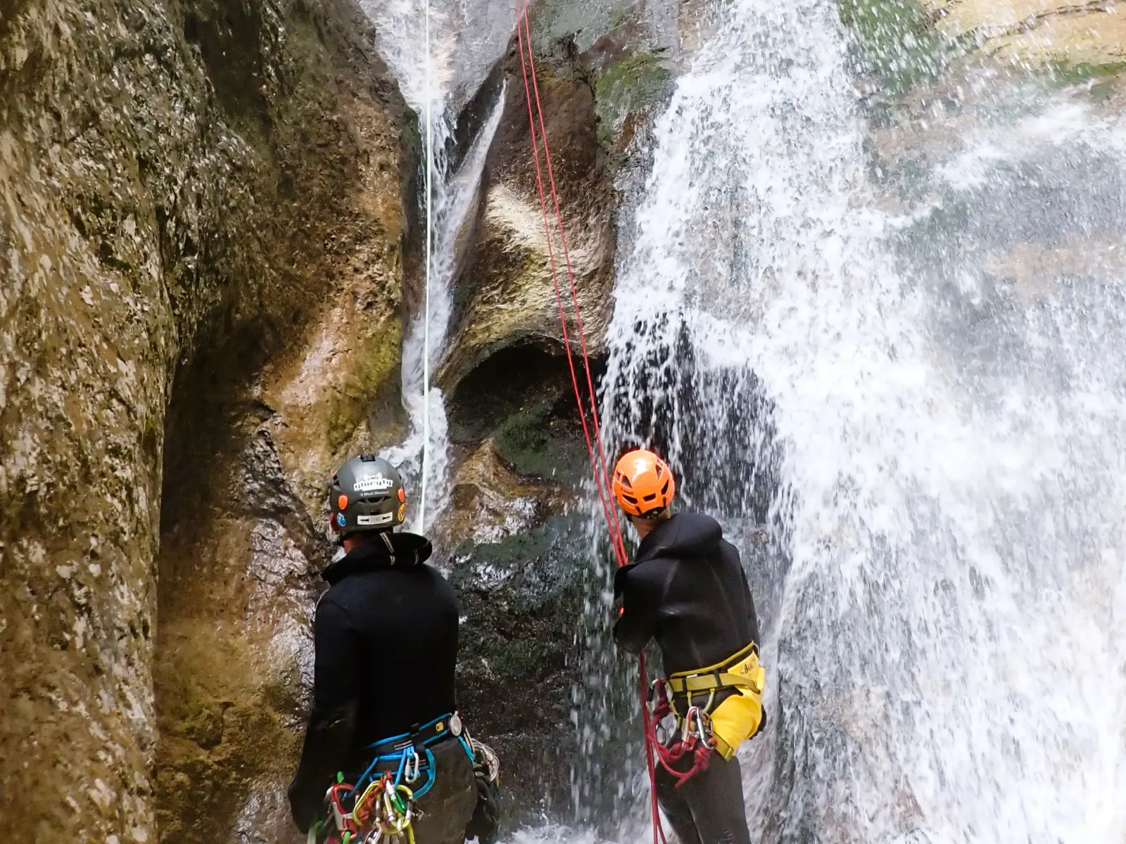 Ein Canyonaut wird von einem anderen in einem Wasserfall abgeseilt.