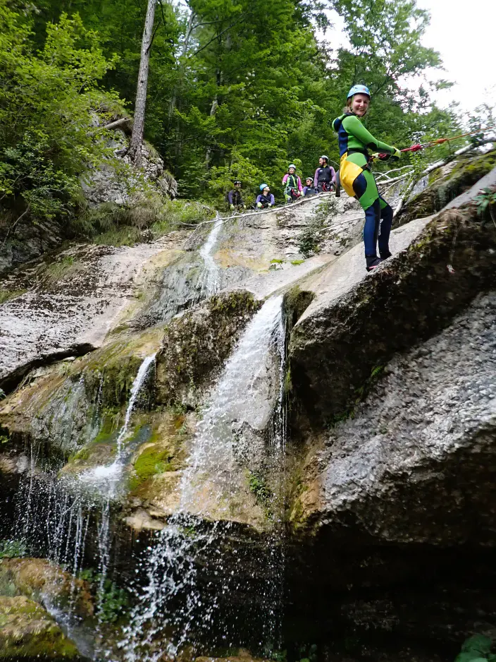 Eine Canyonautin beim Abseilen neben einem Wasserfall.