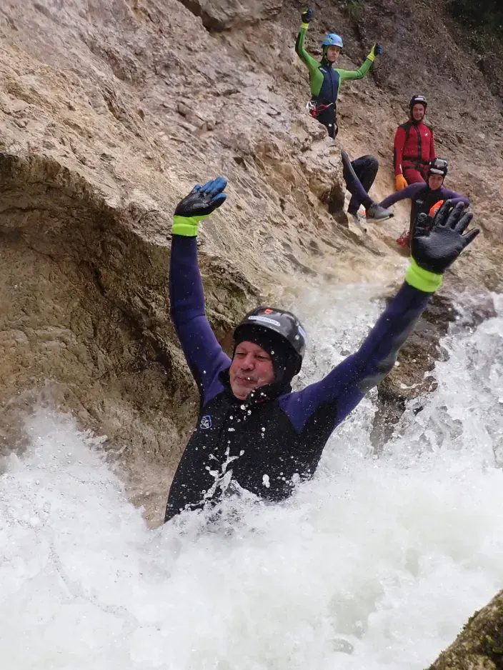 Eine Person rutscht mit den Armen in der Luft durch schäumendes Wasser in einem Canyon.