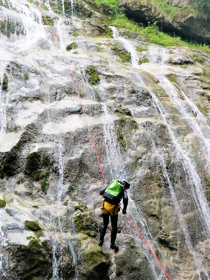 Ein Canyonaut seilt sich an einem sehr breiten Wasserfall ab.
