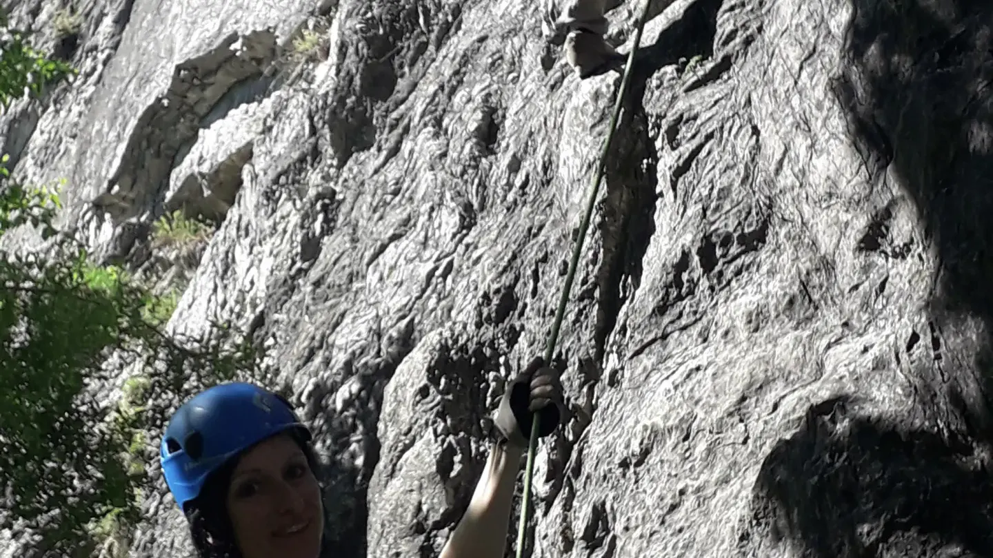 Eine Person klettert an der Felswand und eine weitere Person sichert sie.