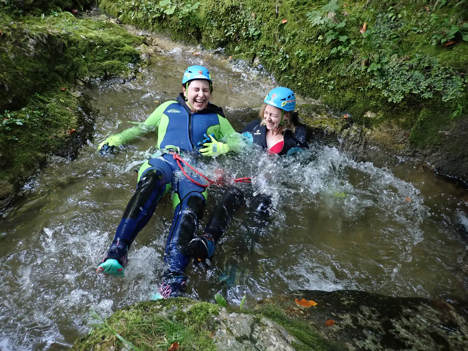 Zwei Personen in Canyoning-Ausrüstung liegen lachend im Gebirgsbach.