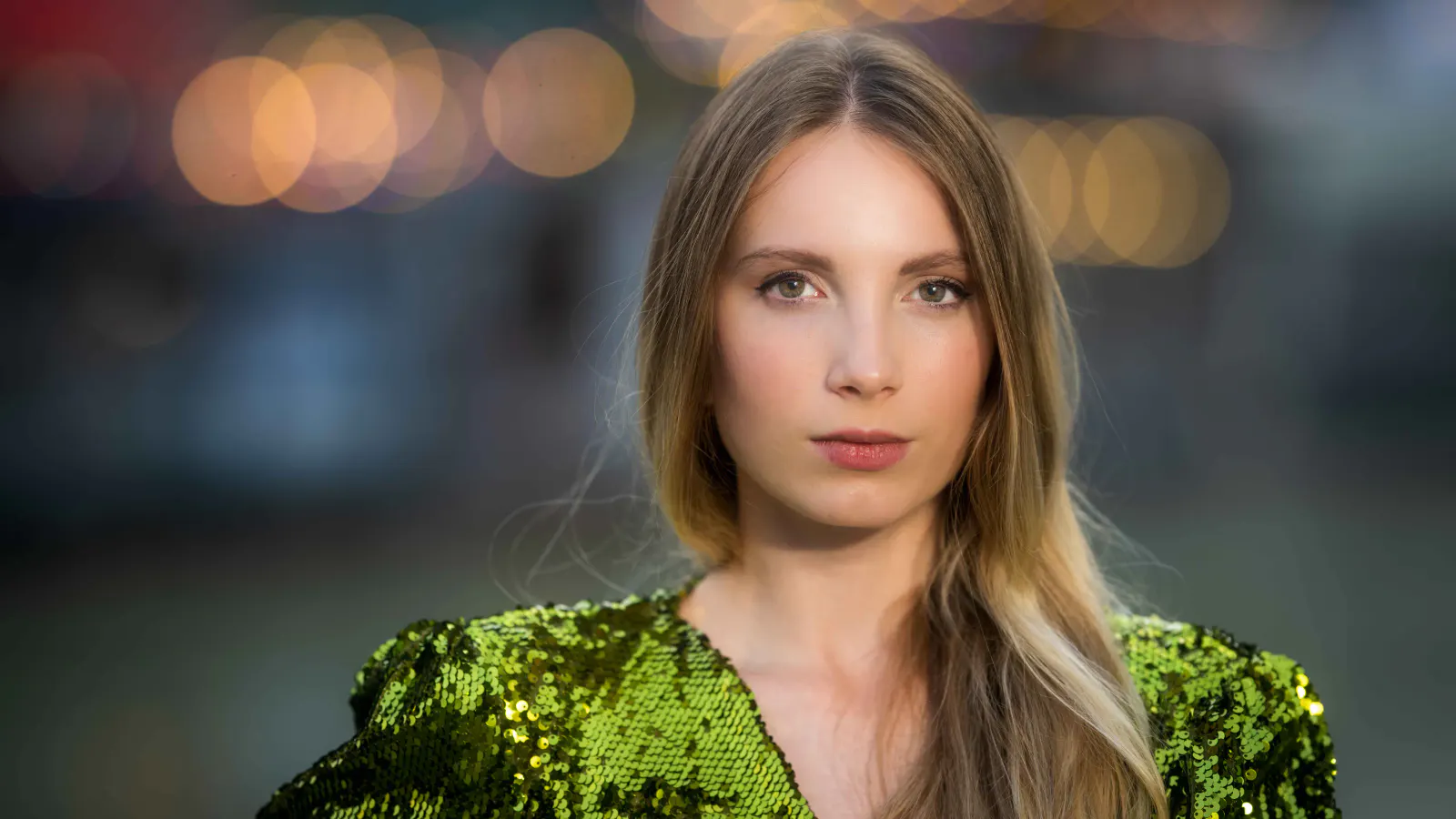 Nächtliches Portrait einer Frau im grünen Outfit vor unscharfen Lichtern der Stadt.