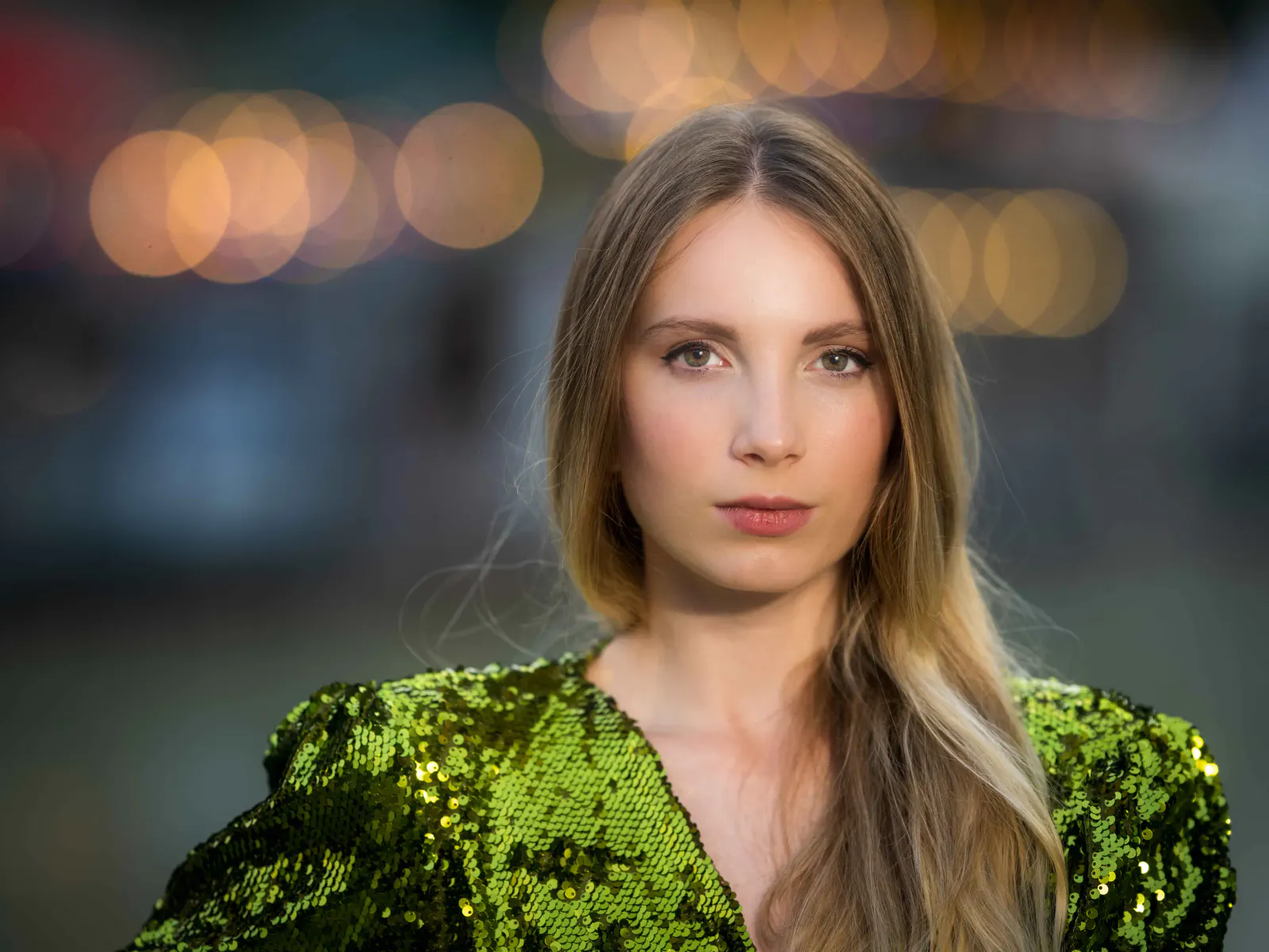 Nächtliches Portrait einer Frau im grünen Outfit vor unscharfen Lichtern der Stadt.