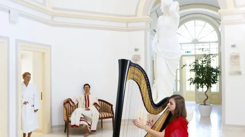 Eine Harfespielerin und zwei Gäste im Bademantel im historischen Teil des Wellnessbereiches im Rimske Terme Hotel Rimski dvor