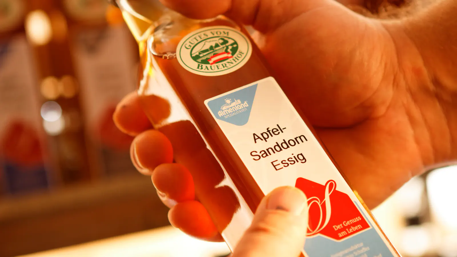 Eine Flasche Spezialitätenessig der Sorte Apfel-Sanddornessig in Händen gehalten
