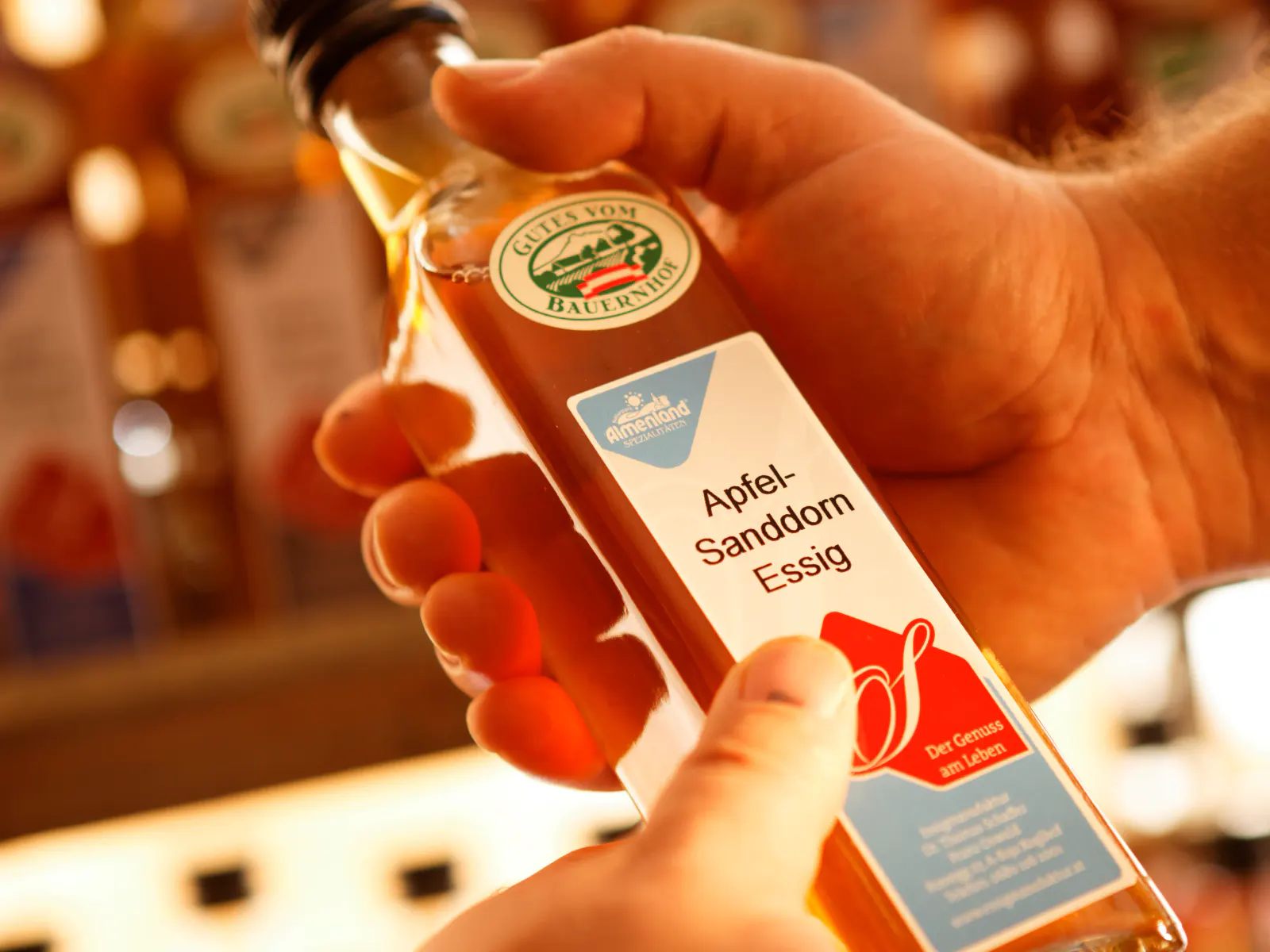 Eine Flasche Spezialitätenessig der Sorte Apfel-Sanddornessig in Händen gehalten
