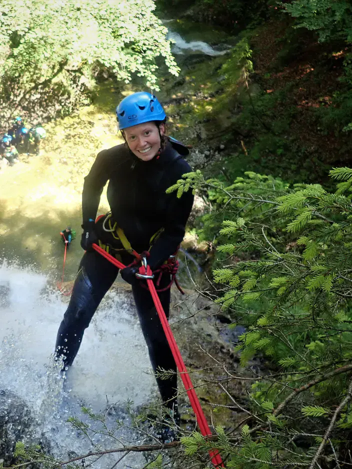 Eine Canyonautin steht an einem Vorsprung bevor sie sich einen hohen Wasserfall abseilt.