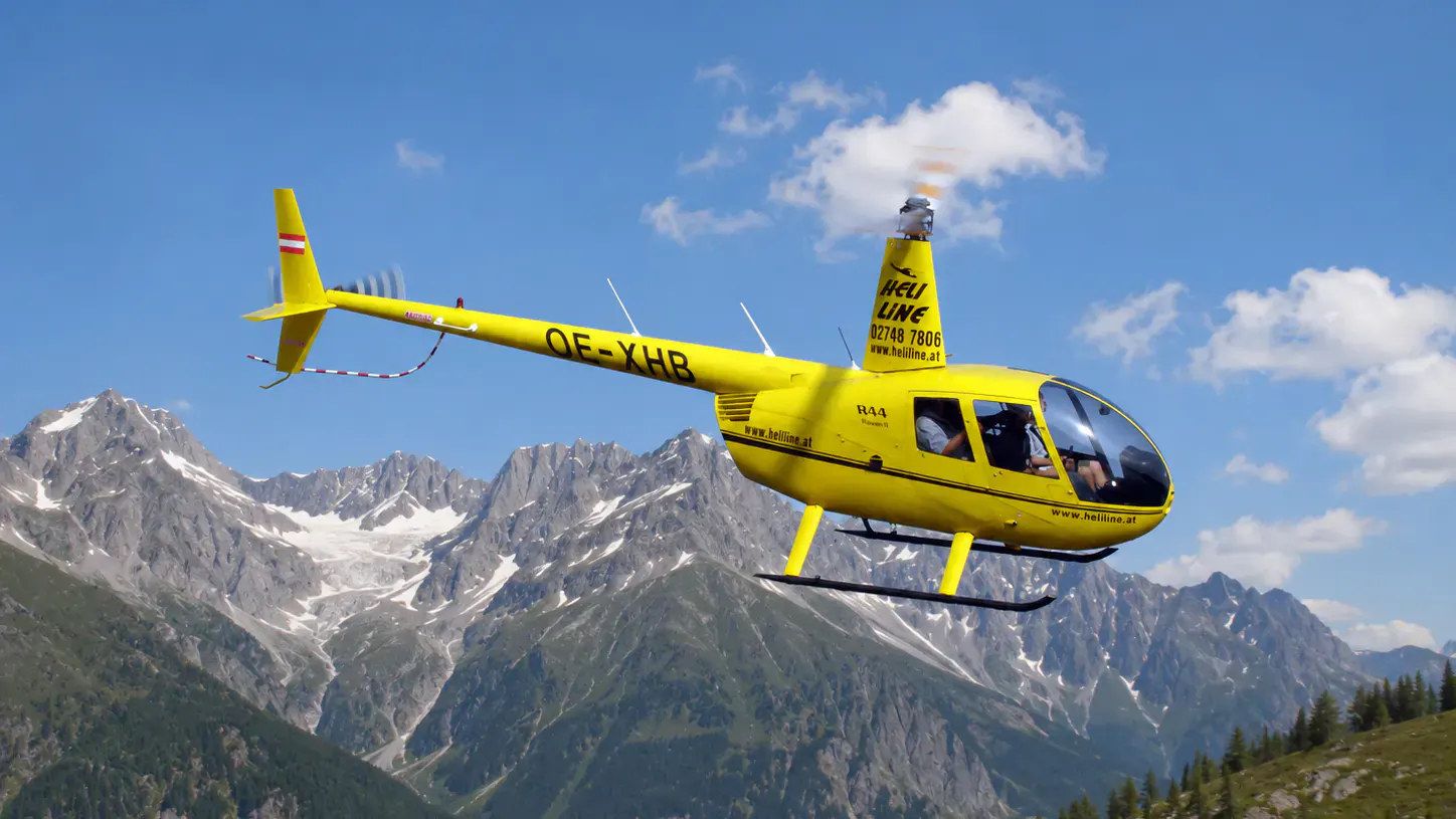 Helikopter in der Luft. Im Hintergund ein Berg.