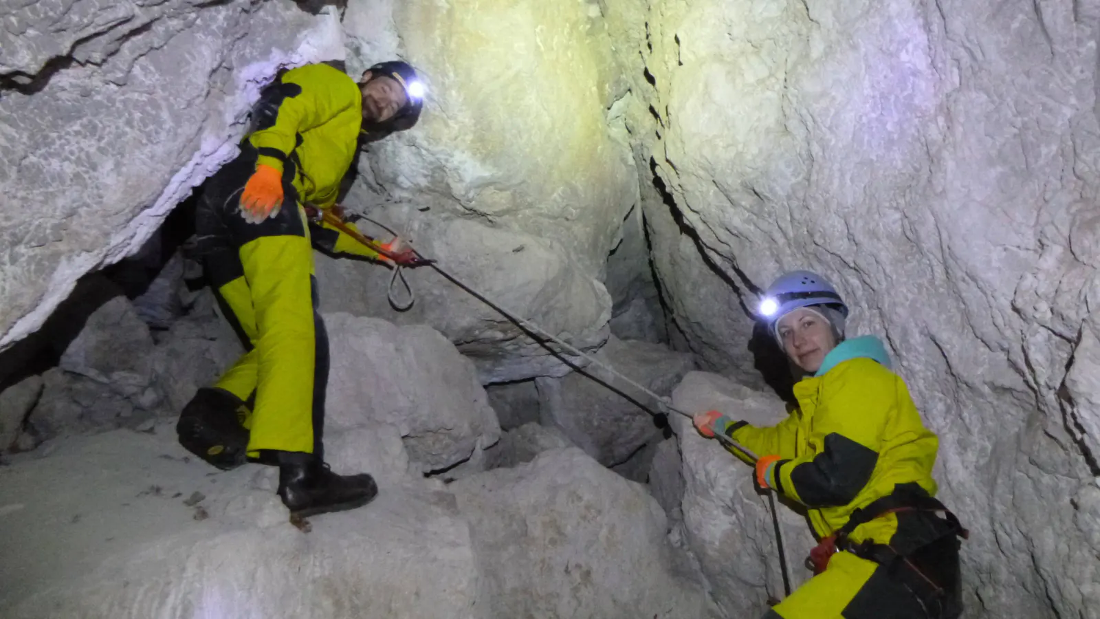 Zwei Personen in Höhlenanzügen seilen sich in der Höhle ab.