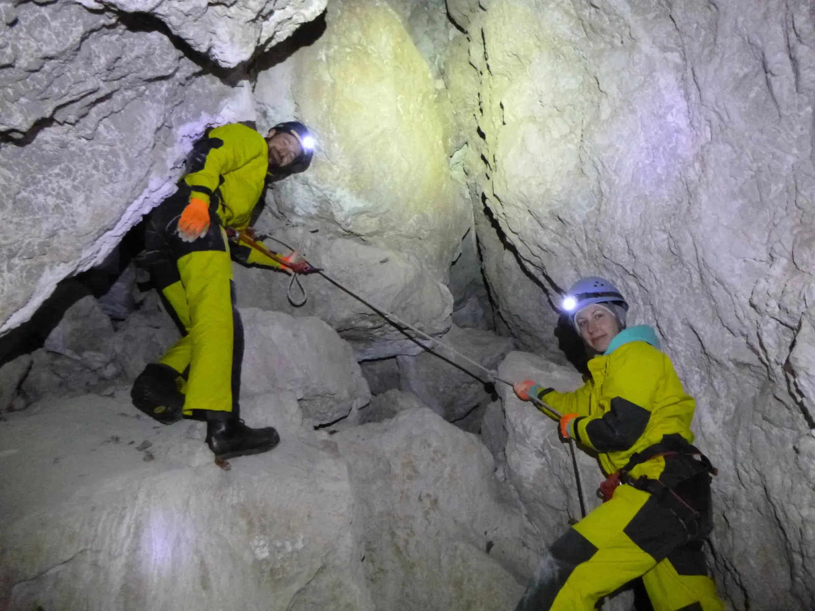 Zwei Personen in Höhlenanzügen seilen sich in der Höhle ab.