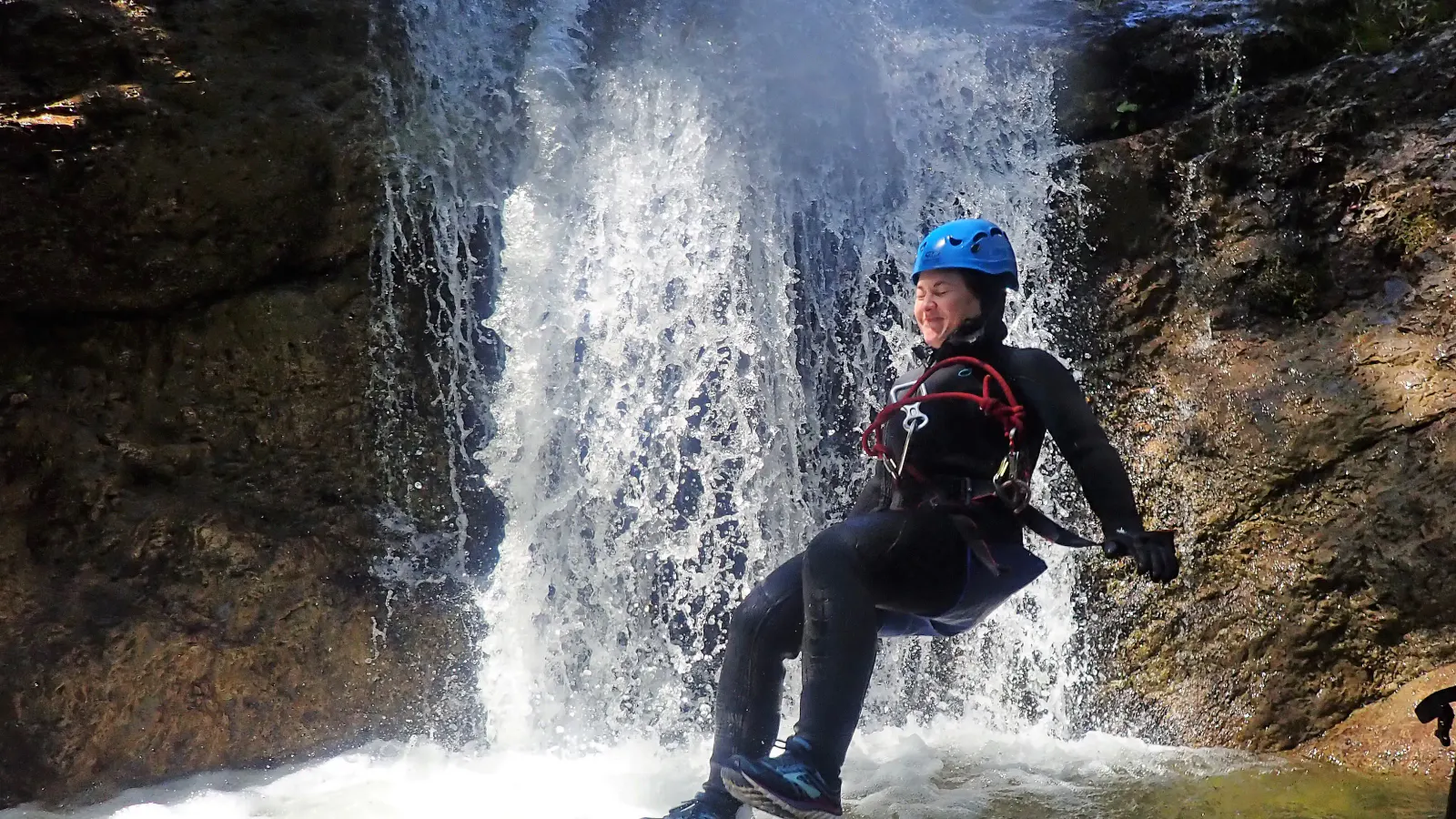 Eine Person springt vor einem Wasserfall ins Wasser.