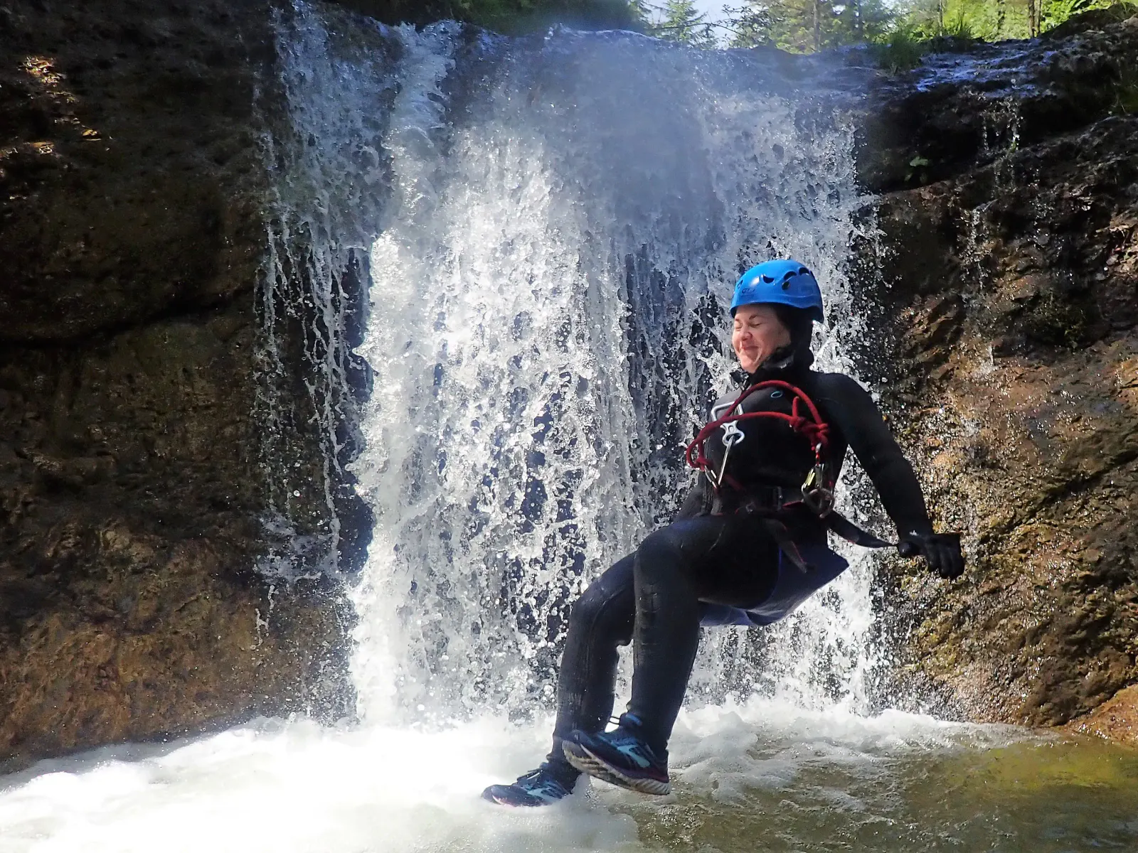 Eine Person springt vor einem Wasserfall ins Wasser.
