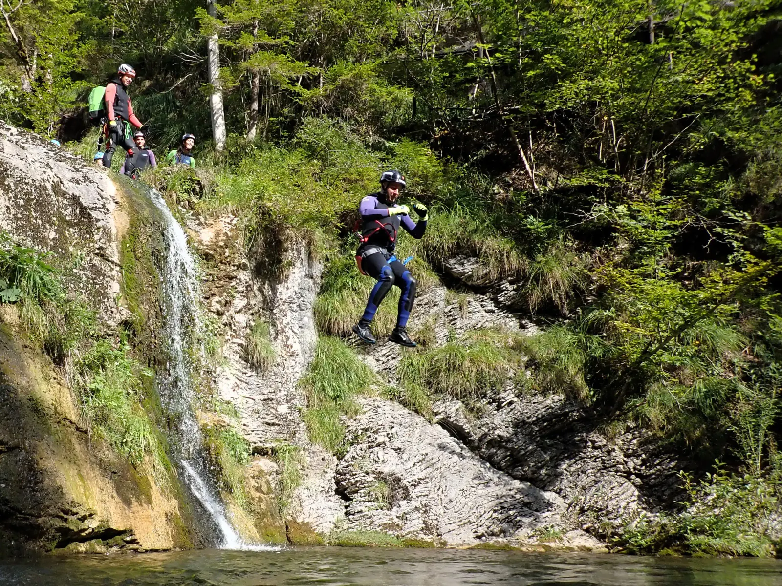 Eine Person in Canyoningausrüstung springt mehrere Meter ins Wasser.
