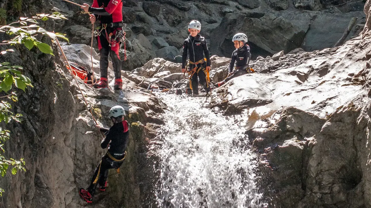 Kind wird von Guide neben Wasserfall abgeseilt