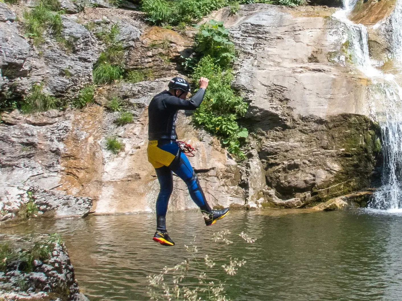 Eine Person während dem Sprung ins Wasser mit einem Wasserfall im Hintergrund.