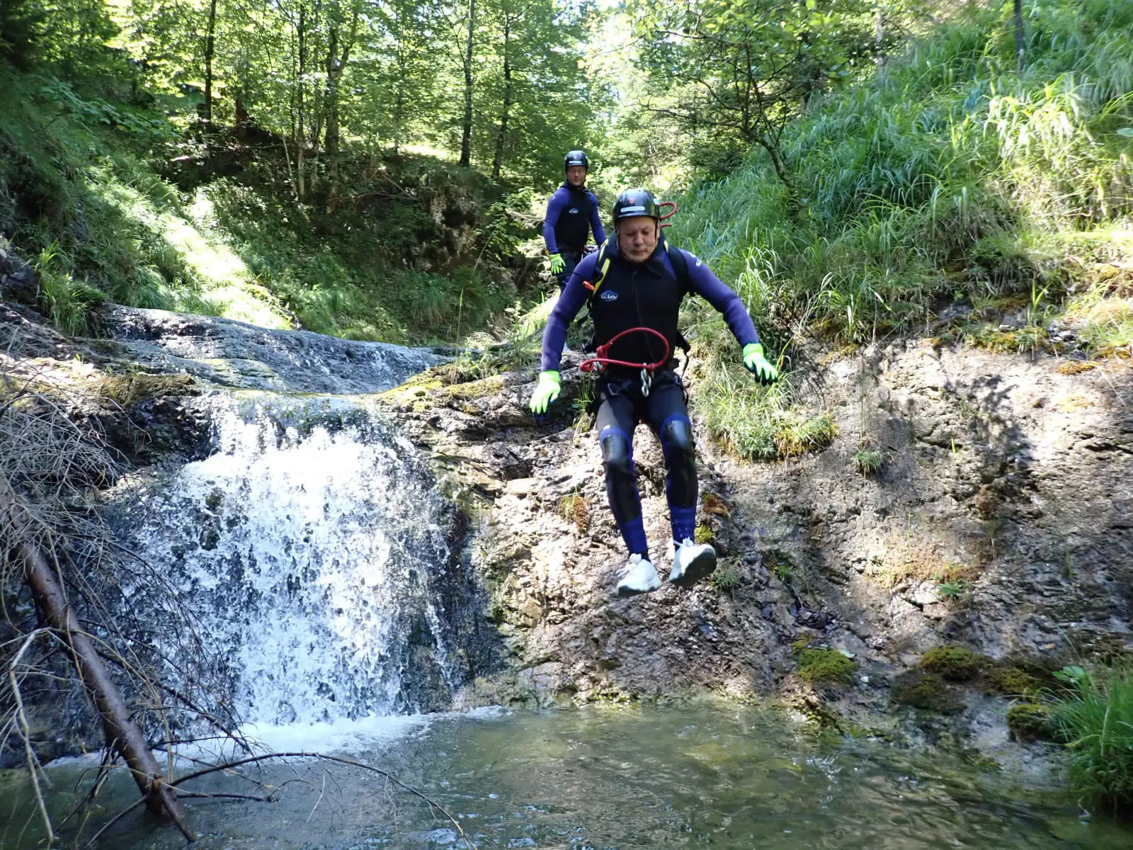 Eine Person springt von einem Vorsprung, im Hintergrund ein kleiner Wasserfall.