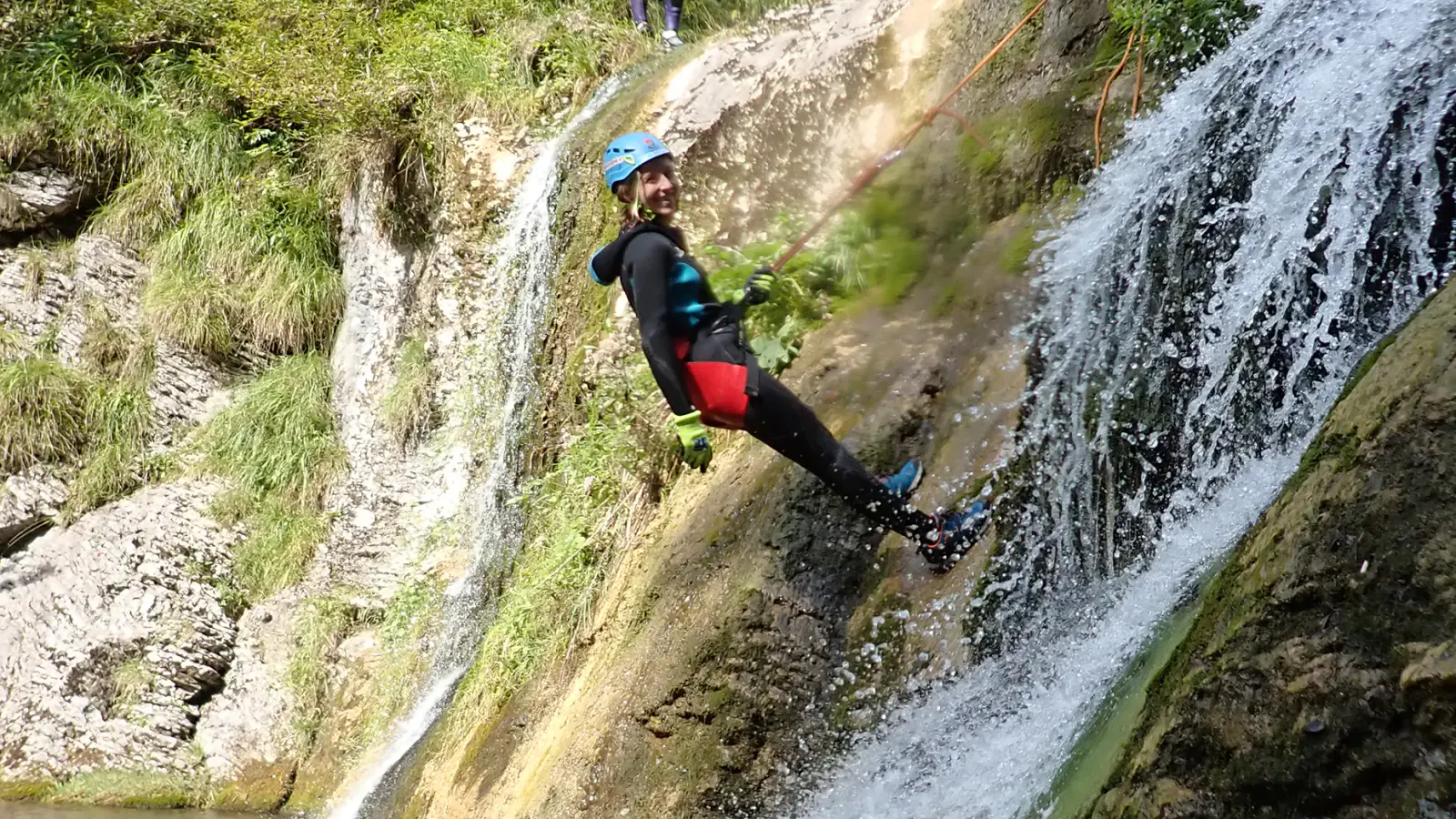 Eine Person wird neben einem Wasserfall abgeseilt.