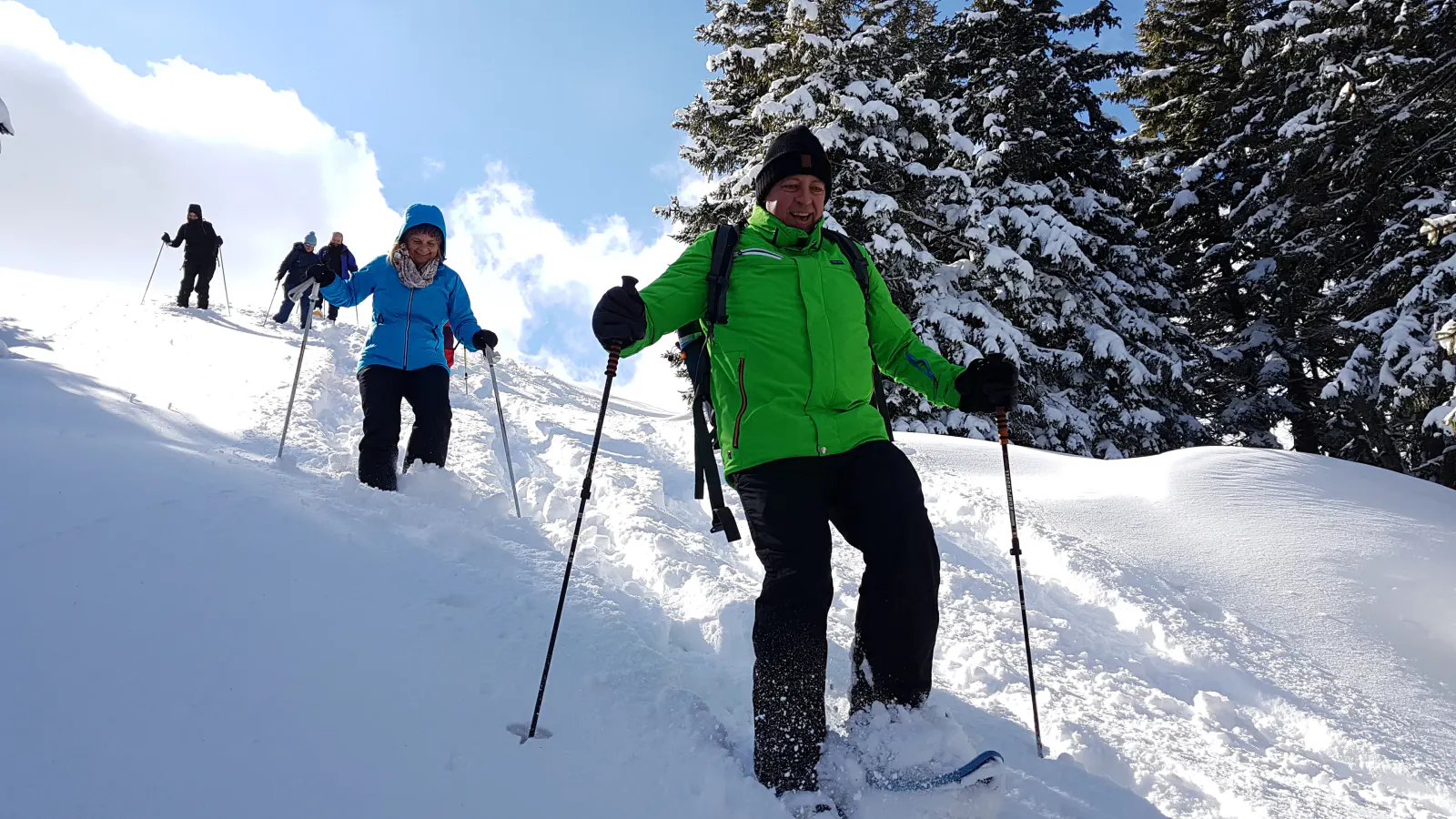 Personen, die lachend mit Schneeschuhen einen Hang hinunterlaufen.