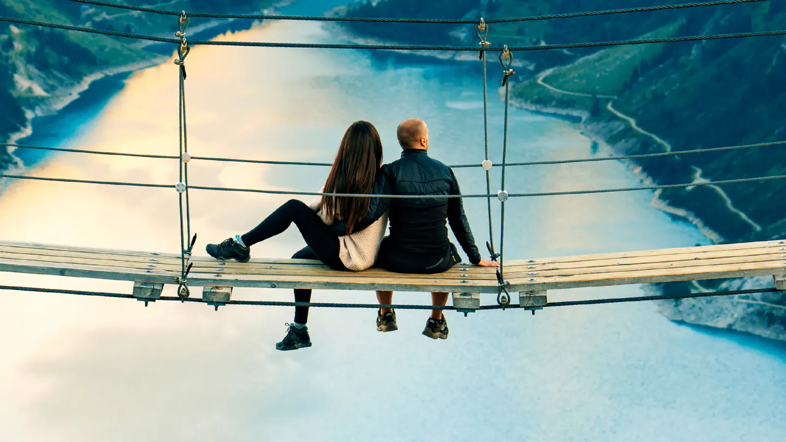 Ein Paar sitzt auf einer Hängebrücke über einem See