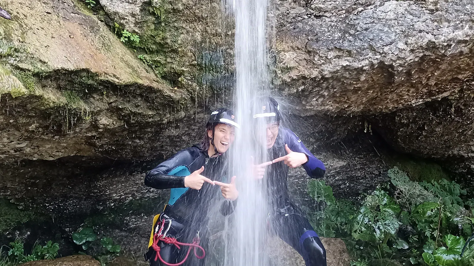 Zwei Personen, die lachend unter einem Wasserfall stehen