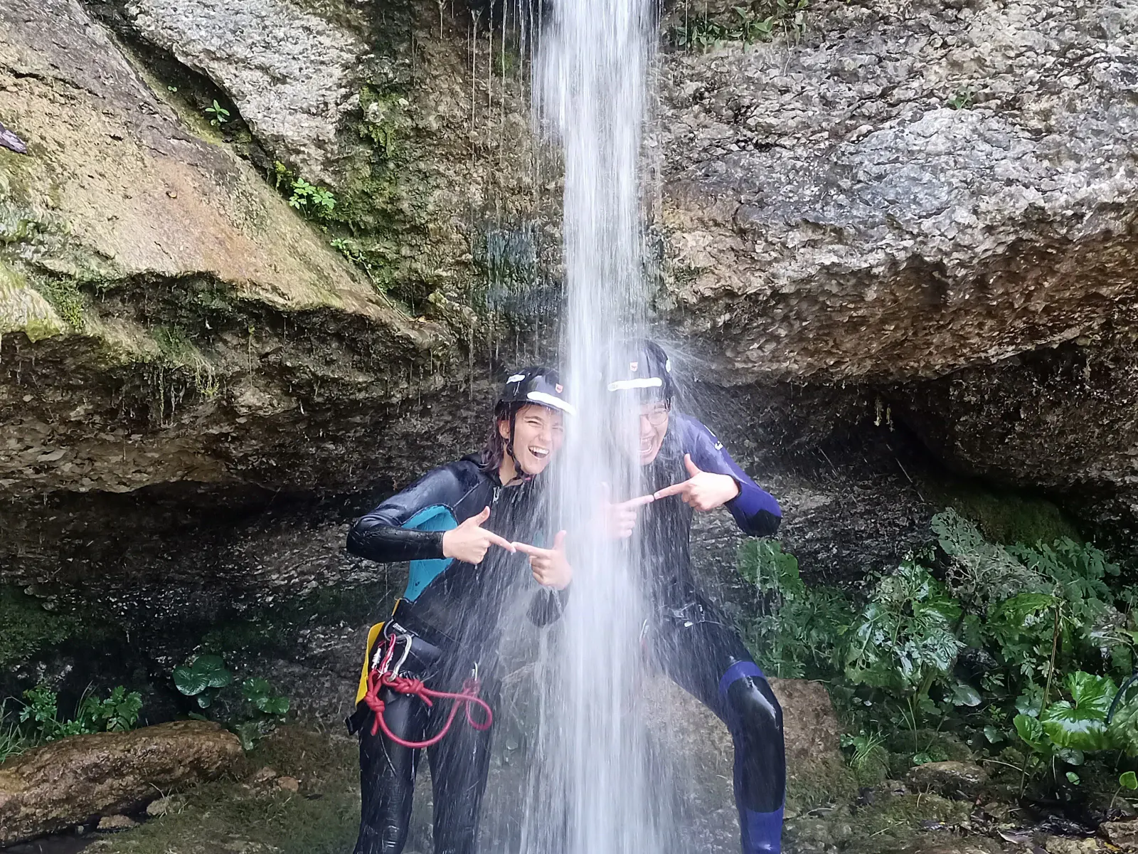 Zwei Personen, die lachend unter einem Wasserfall stehen