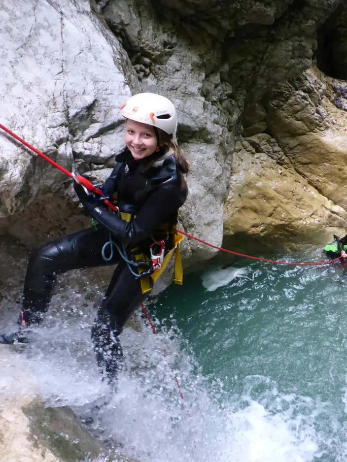 Eine Canyonautin seilt sich ab, einer wartet im Wasser und einer klettert.