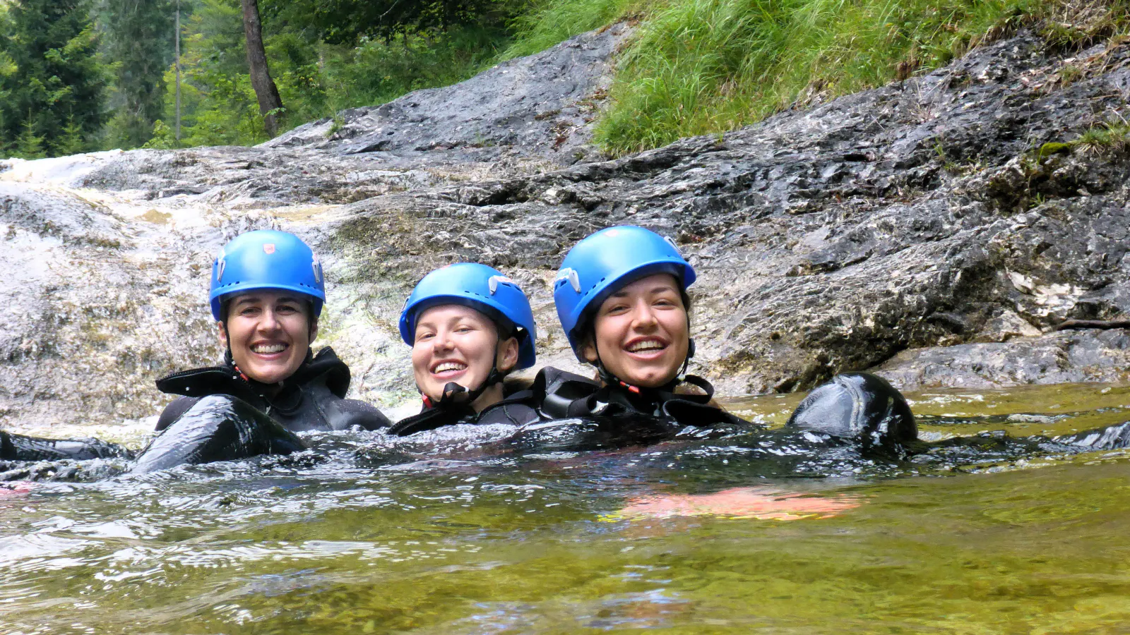 Drei Personen im Wasser mit Felsen im Hintergrund.