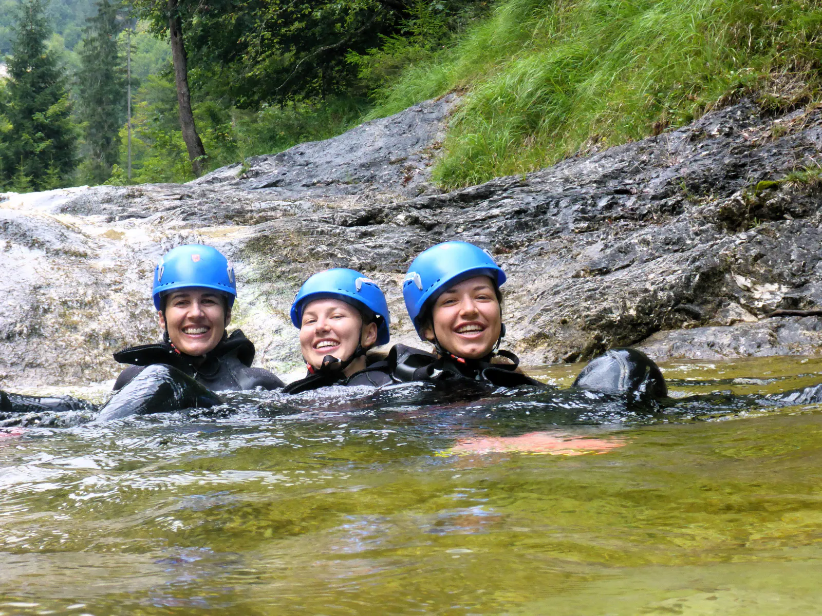 Drei Personen im Wasser mit Felsen im Hintergrund.