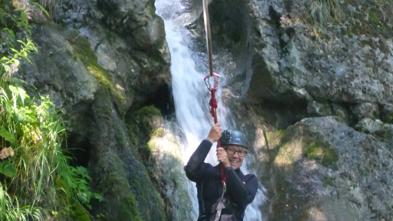Eine Person hängt an einem Seil mit Wasserfall im Hintergrund.