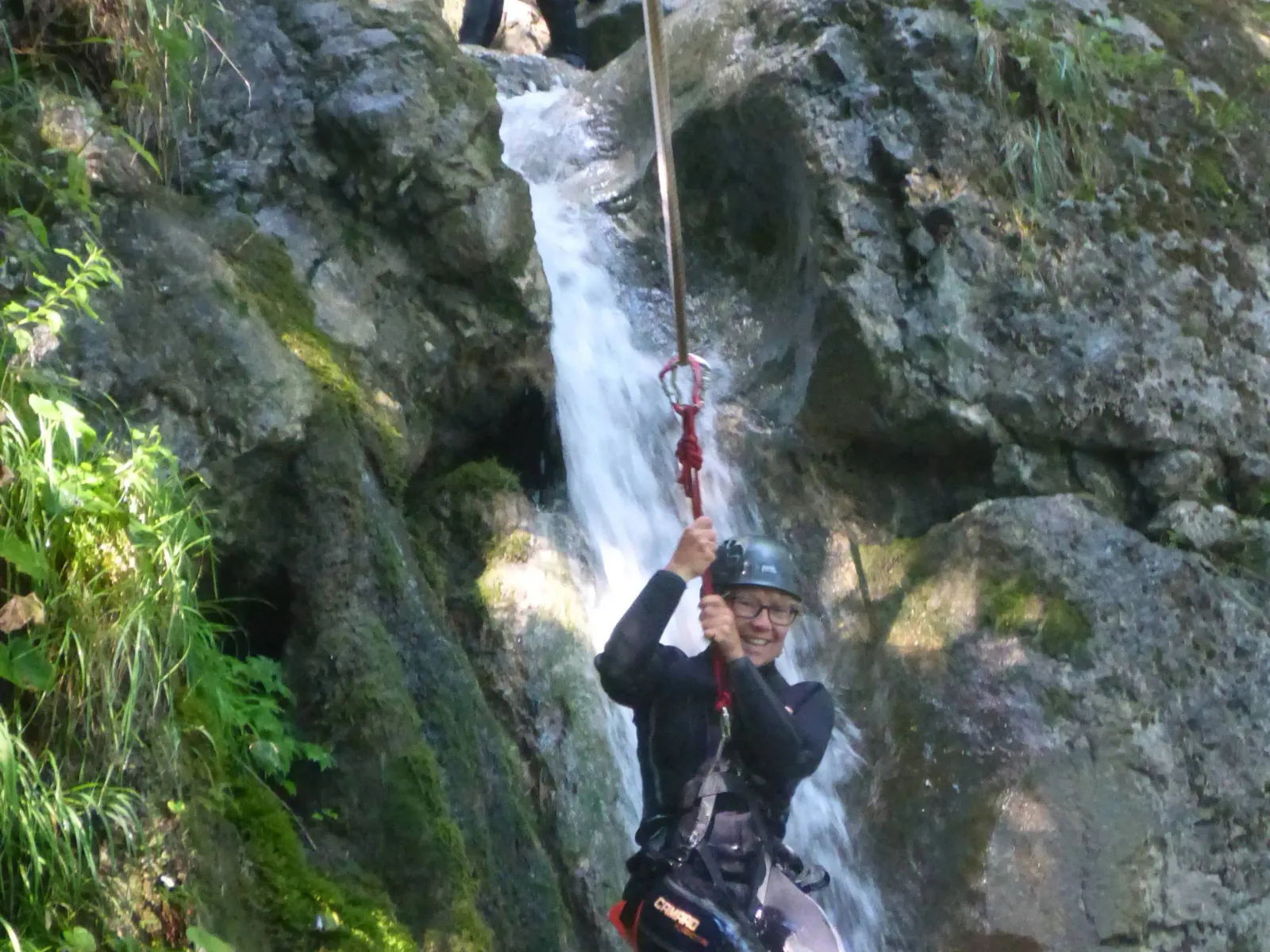 Eine Person hängt an einem Seil mit Wasserfall im Hintergrund.