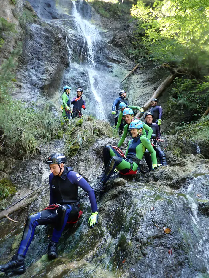 Eine Gruppe Canyonaut:innen in Neoprenanzügen, Helmen und Gurten mit einem Wasserfall im Hintergrund.
