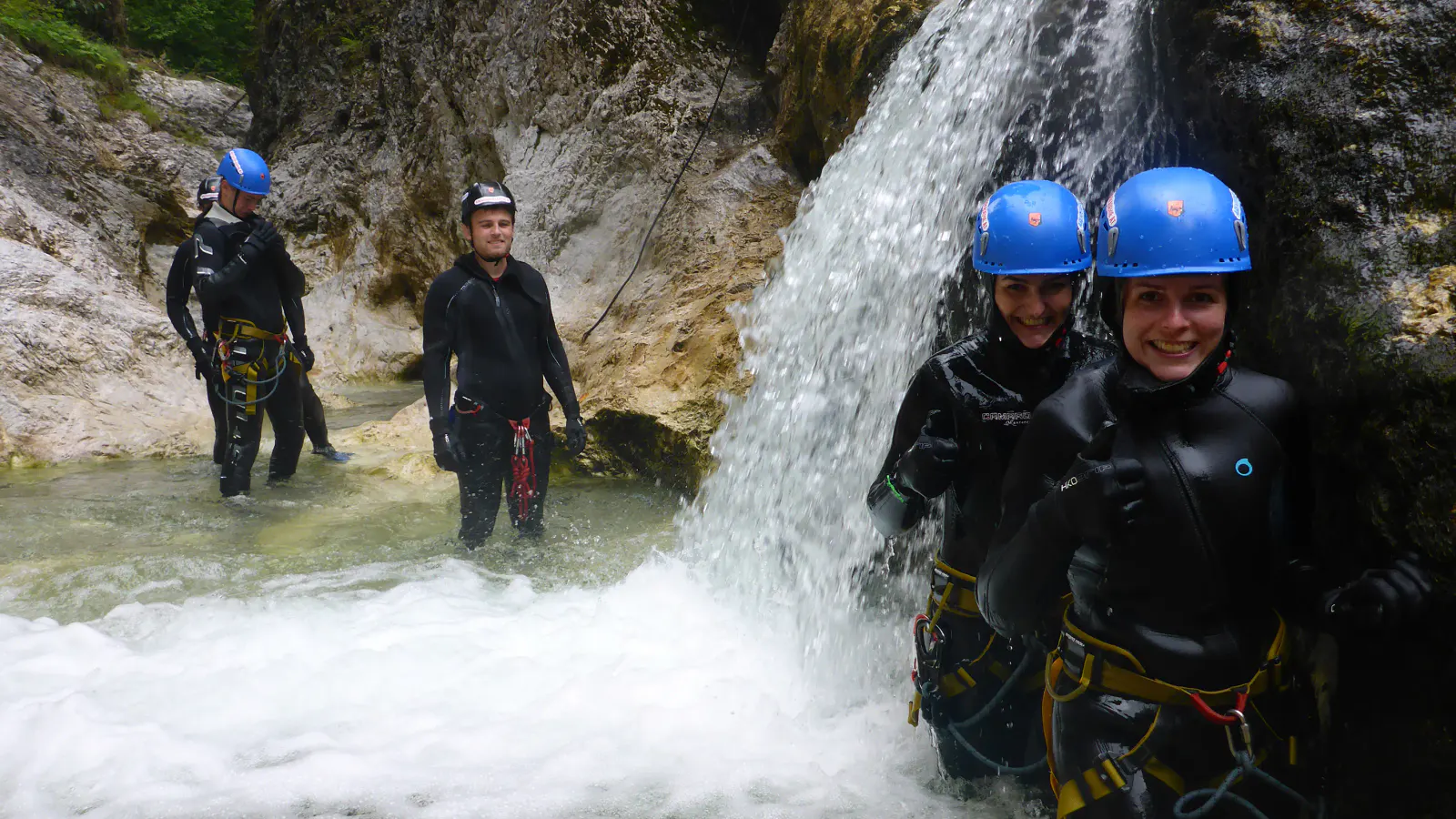 Canyonaut:innen beim Passieren einer Stelle mit tieferem Wasser und einem Wasserfall.