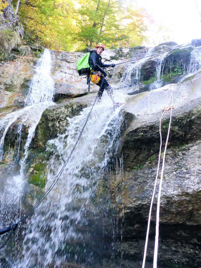 Eine mit Neoprenanzug und Kletterausrüstung ausgestattete Person seilt sich entlang eines Wasserfalls ab.