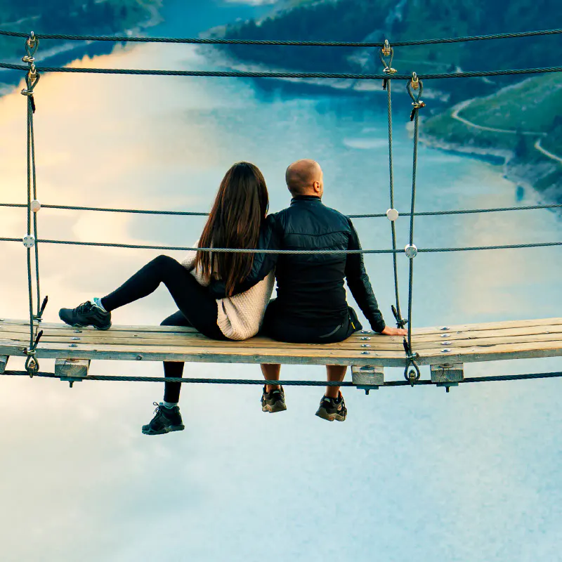 Ein Paar sitzt auf einer Hängebrücke über einem See